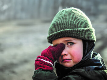 Ein weinendes Kind mit Mütze und roten Handschuhen wischt sich eine Träne aus dem Augenwinkel.