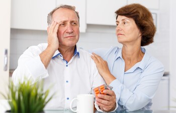Mann hält Tabletten, während Partnerin ihn bei beginnender Demenz beruhigt