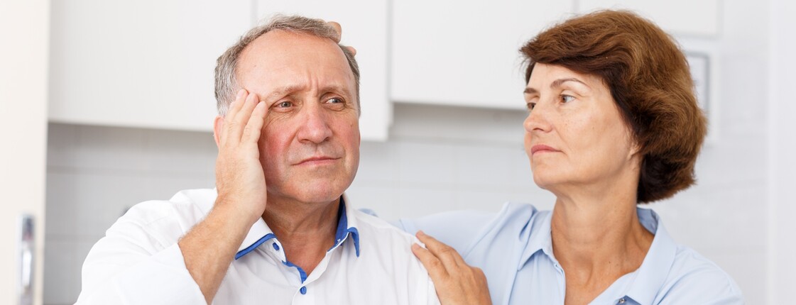 Mann hält Tabletten, während Partnerin ihn bei beginnender Demenz beruhigt