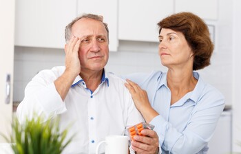 Mann hält Tabletten, während Partnerin ihn bei beginnender Demenz beruhigt