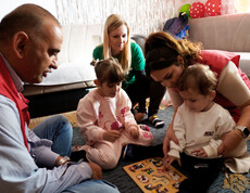 Zwei Kinder setzen Holzpuzzleteile ein, umgeben von Betreuungspersonen
