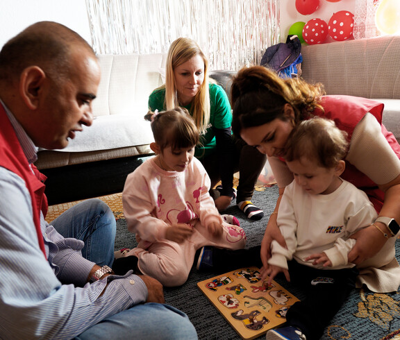 Zwei Kinder setzen Holzpuzzleteile ein, umgeben von Betreuungspersonen