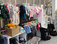 Eine Kleiderstange voller Babykleidung sowie zwei Kindersitzen für das Auto.