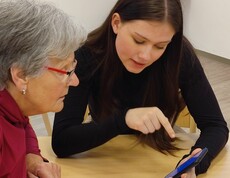 Schülerin erklärt einer Seniorin das Smartphone