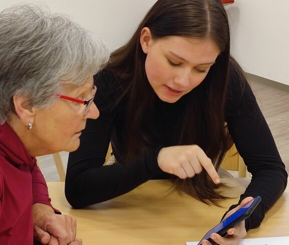 Schülerin erklärt einer Seniorin das Smartphone