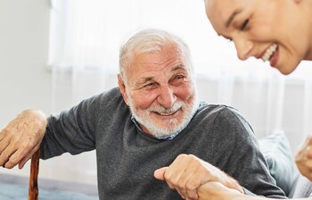 Eine Pflegerin hilft einem alten Mann, beide lachen