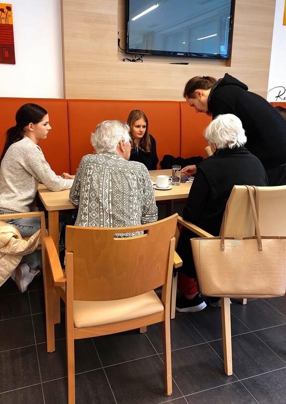 Schülerinnen und Seniorinnen reden an einem Tisch