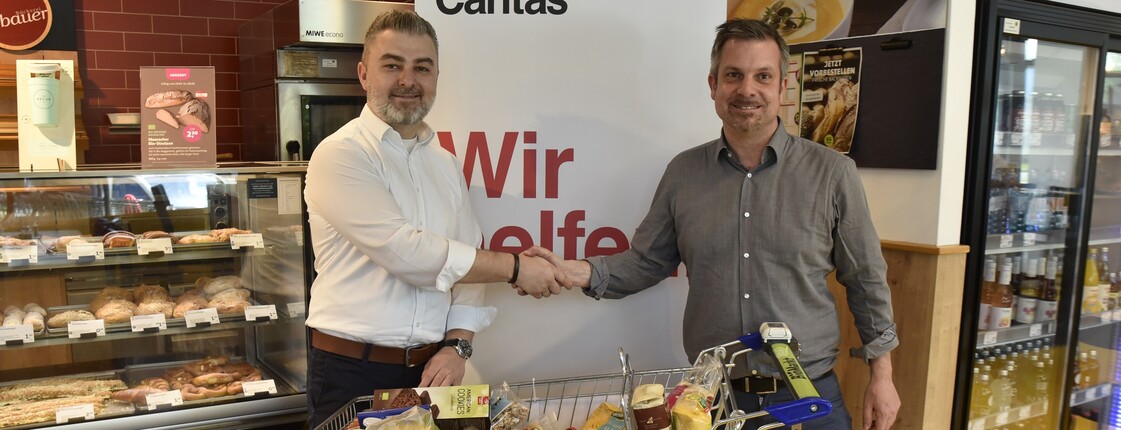 Zwei Männer stehen vor einem Einkaufswagen und schütteln sich die Hände.