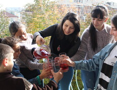 Eine Betreuerin schenkt einer Gruppe Kinder und Jugendlicher roten Saft aus einer Glaskaraffe aus.