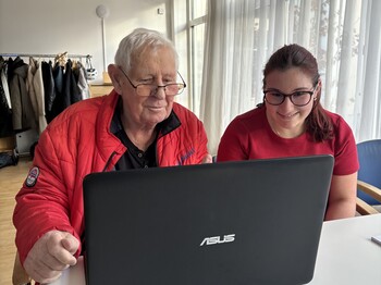 Eine junge Frau und ein älterer Mann arbeiten gemeinsam an einem Laptop