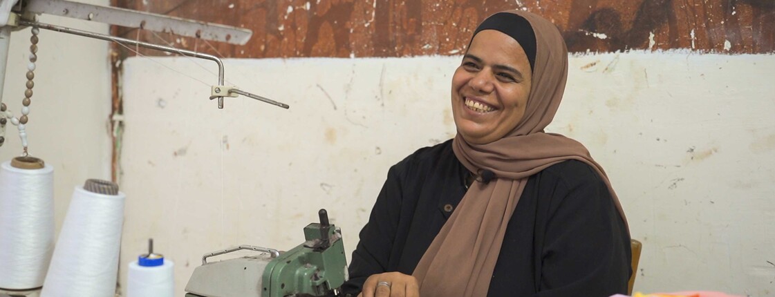 Eine ägyptische Frau mit einer Nähmaschine lacht herzlich.