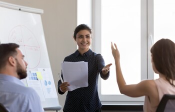 Eine Lehrerin unterrichtet an der Tafel, Schülerin hebt die Hand