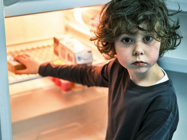 Ein kleiner Junge steht vor einem fast leeren Kühlschrank