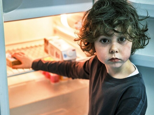 Ein kleiner Junge steht vor einem fast leeren Kühlschrank