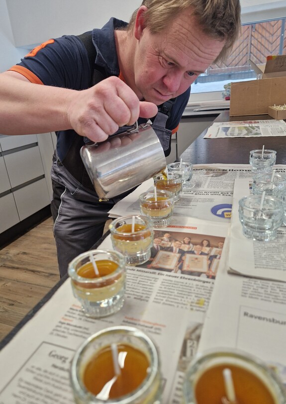 Ein Mann gießt Wachs in Teelichtergläser