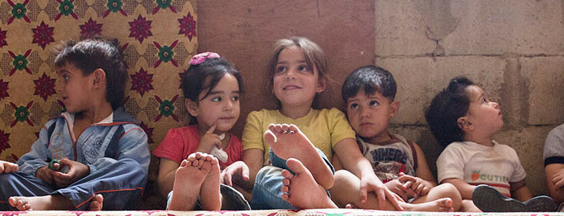 Kinder im Libanon sitzen aufgereiht barfuss an der Wand eines Zimmers