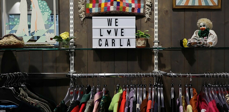 Ein Regal mit einem Schild au fem "We Love Carla" steht. Darunter befindet sich eine Kleiderstange.
