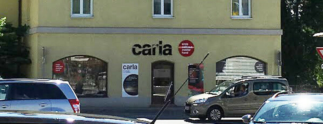 Der Carla Shop Aigen von außen. Ein gelbes Haus mit Spitzdach. Über dem Eingang ist ein großer "Carla" Schriftzug platziert.