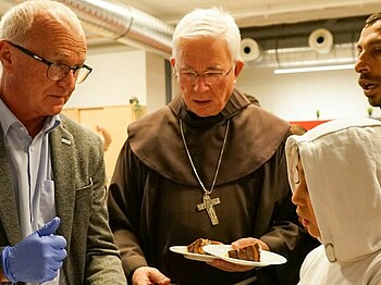 Caritas Direktor Johannes Dines und Erzbischof Franz Lackner verteilen Kuchen an obdachlose Menschen im Haus Elisabeth.