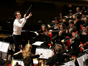 Ein Dirigent steht vor einem Streich-Orchester und dirigiert.